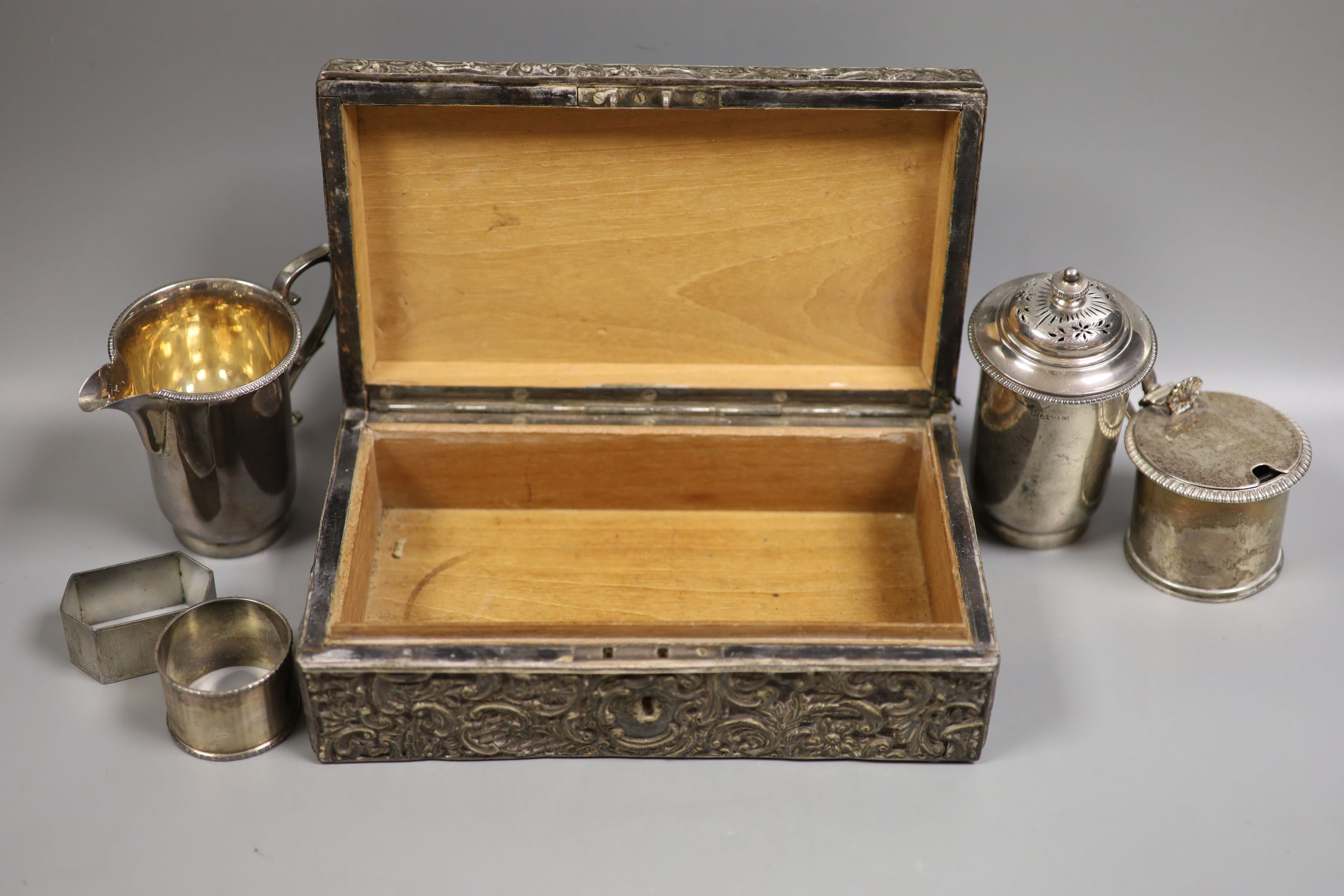 A late Victorian silver mounted leather rectangular jewellery casket, 23.2cm, a silver snuff box, the lid embossed with a wild fowling scene, a George V silver cream jug and pepper, two silver napkin rings and a Victoria